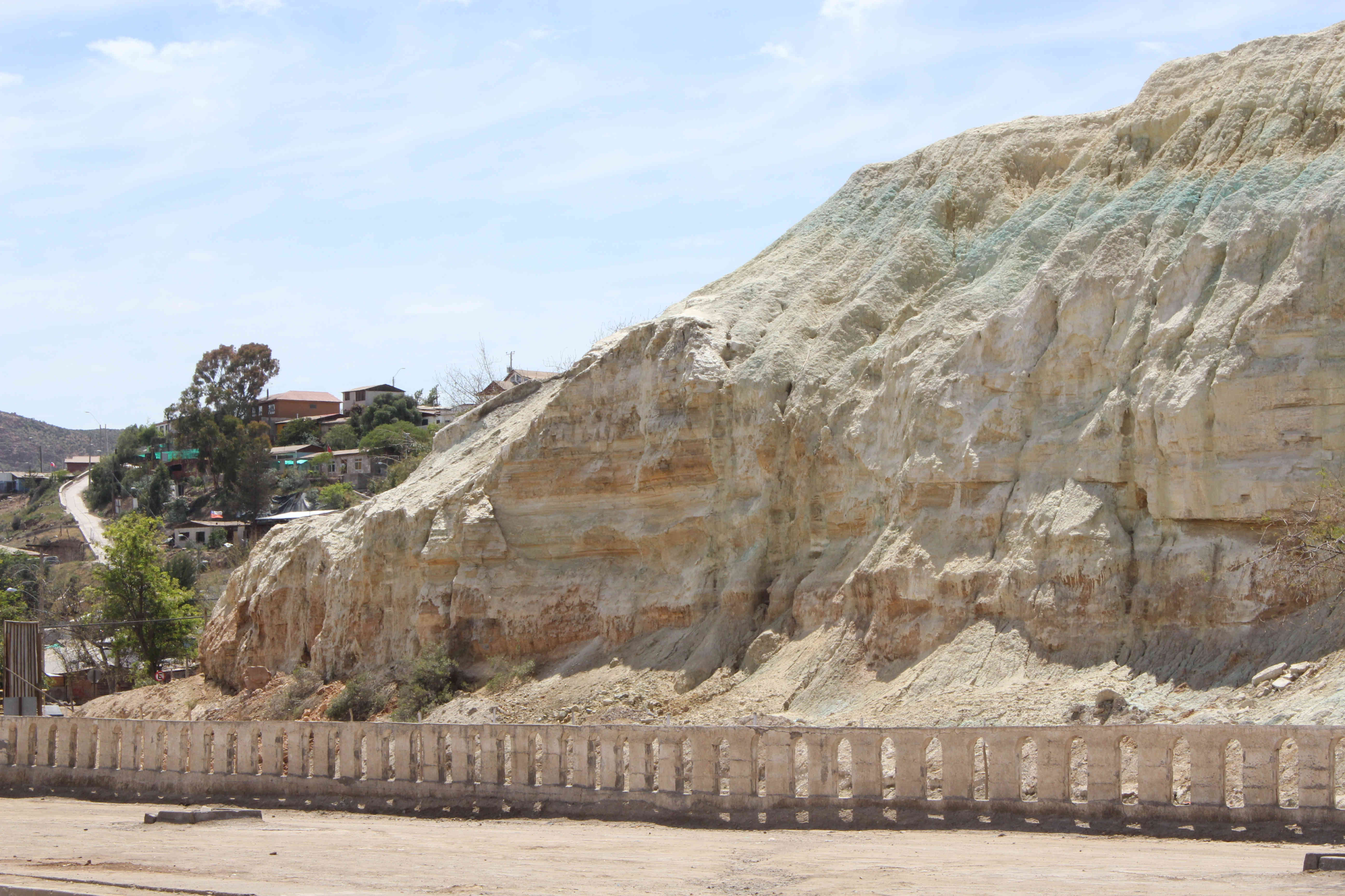 Talud de relave estratificado en Andacollo con capas ocres, blancas y verdes junto a una calle